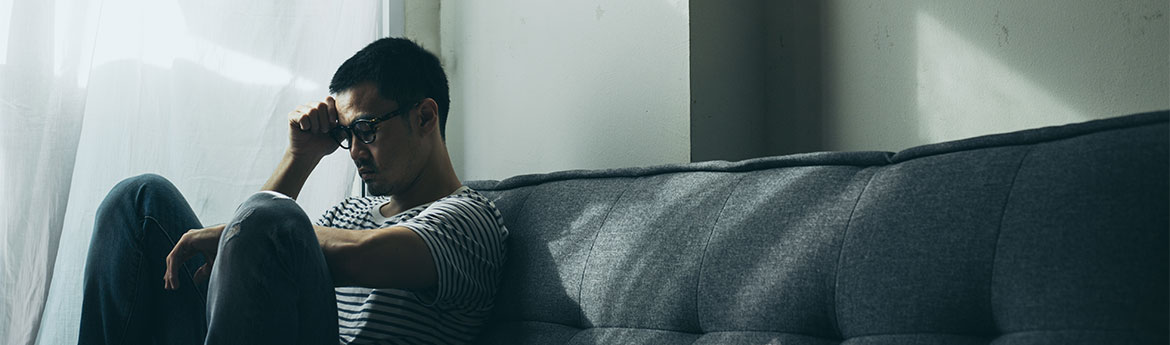 Junger Mann mit Angststörung sitzt alleine auf dem Sofa