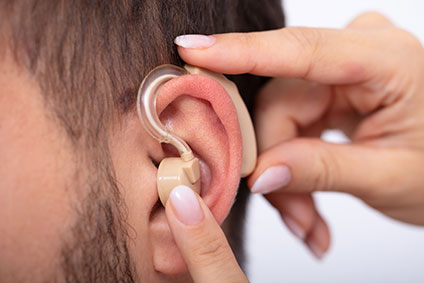 Arzt, der ein Hörgerät in das Ohr eines Patienten einführt.