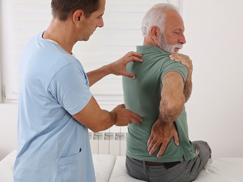 Physiotherapeut behandelt einen Herren bei Rückenschmerzen 